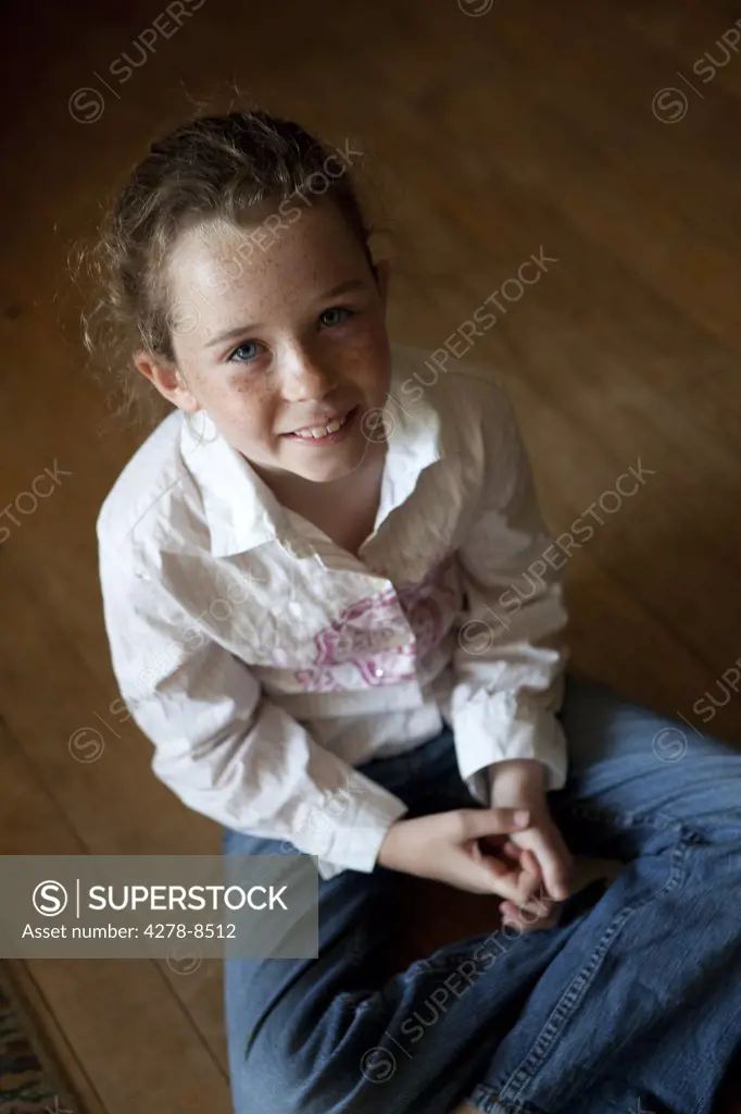 Smiling Girl Sitting on Wood Flooring