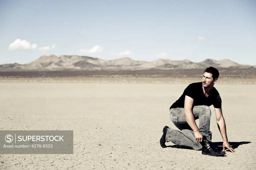Man Crouching in Desert Landscape