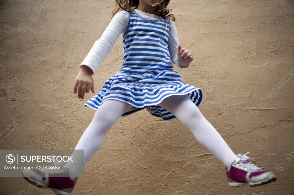 Girl Jumping Mid Air in front of Wall, Cropped
