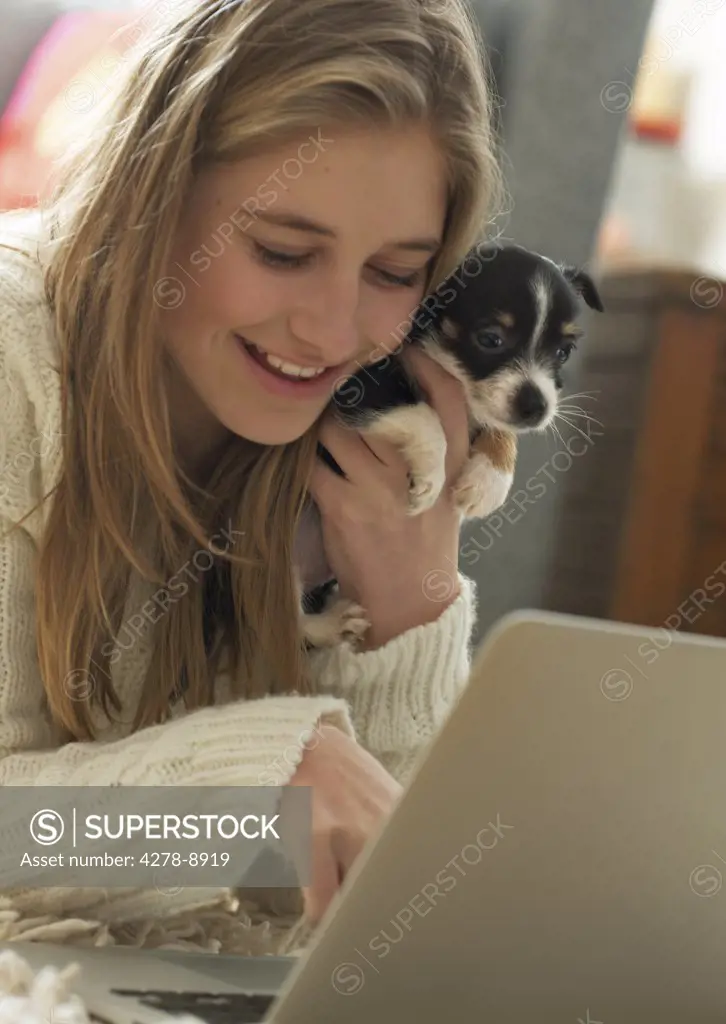 Teenage Girl Hugging Puppy whilst Using Laptop