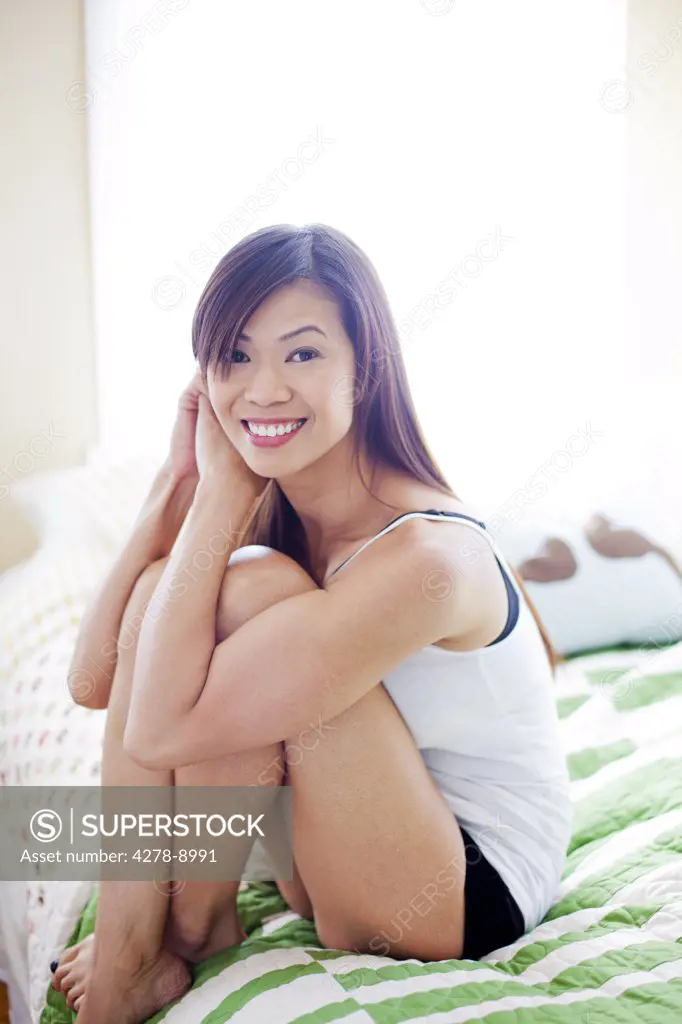 Woman Sitting on Bed with Arms Around Knees