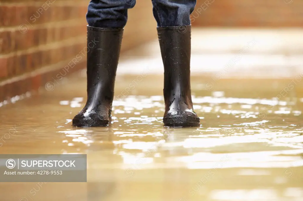 Boy's Legs in Wellington Boots on Flooded Pavement