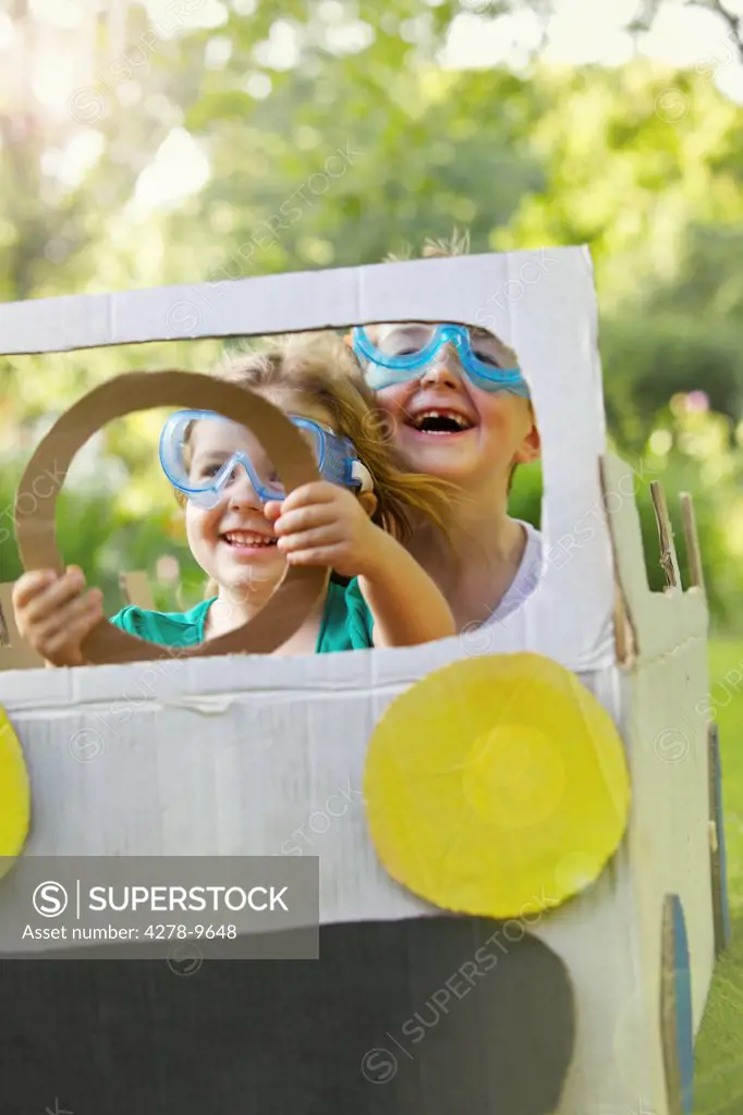 Boy and Girl Wearing Goggles Driving Cardboard Car