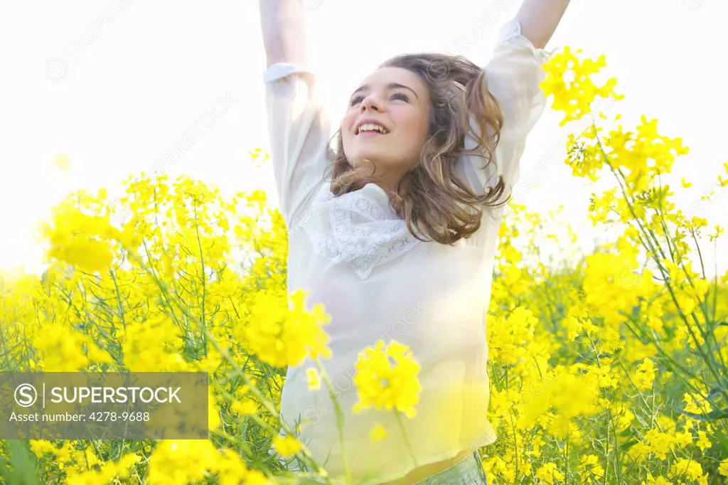 Smiling Teenage Girl with Arms Raised amongst Canola Flowers