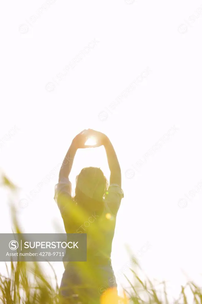 Back View of Woman Standing in a Field with Sun Shining through her Hands
