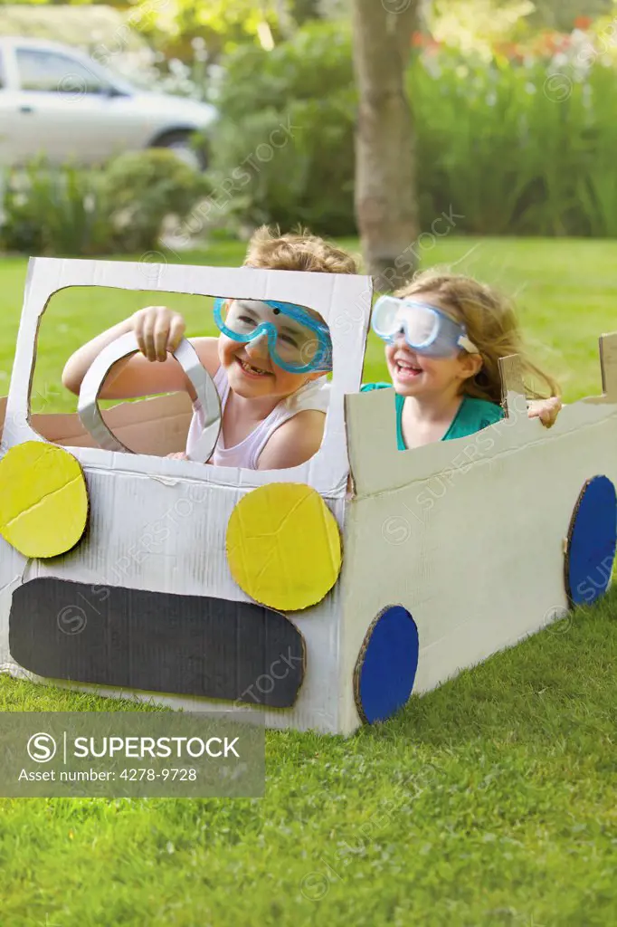 Boy and Girl Wearing Goggles Driving Cardboard Car