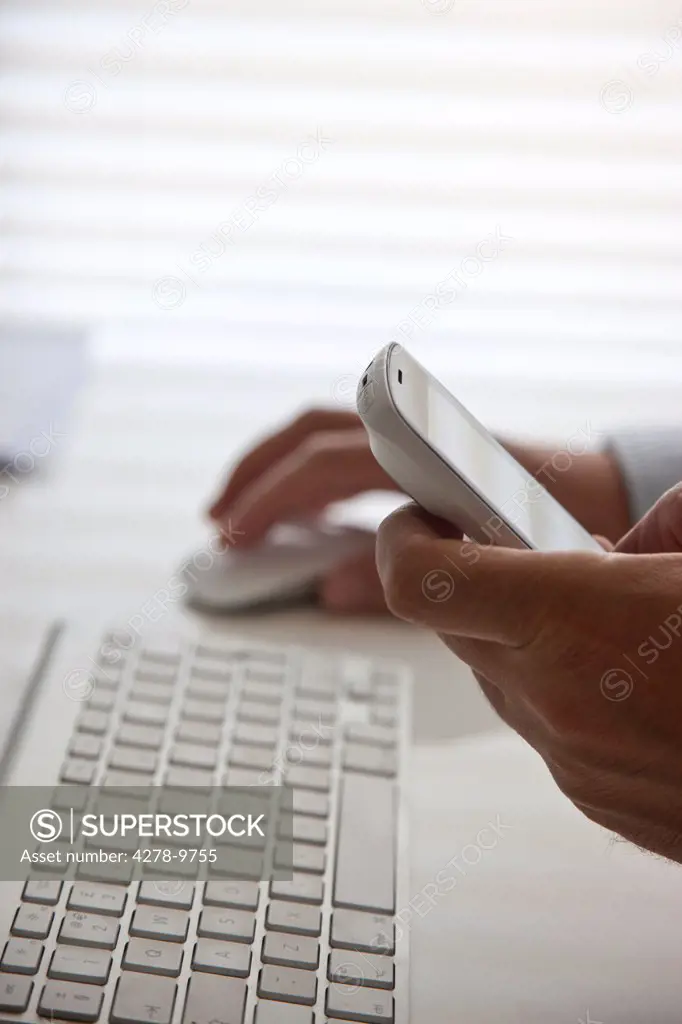 Man Using Computer Mouse and Holding Cell Phone