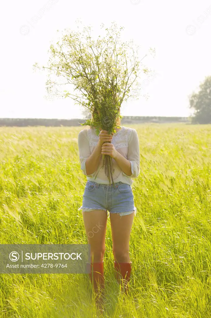 Woman Standing in a Field Holding a Bunch of Wildflowers in front of her Face