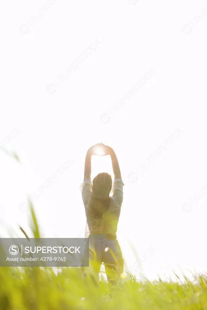 Back View of Woman Standing in a Field with Sun Shining through her Hands