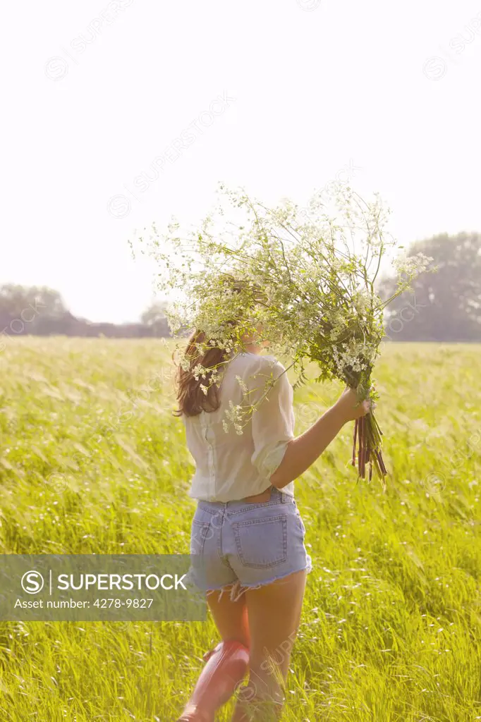 Back View of Young Woman in a Field Holding a Bunch of Wildflowers