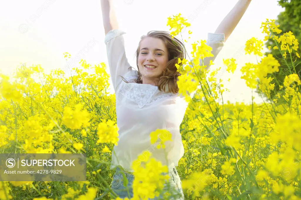 Smiling Teenage Girl with Arms Raised amongst Canola Flowers