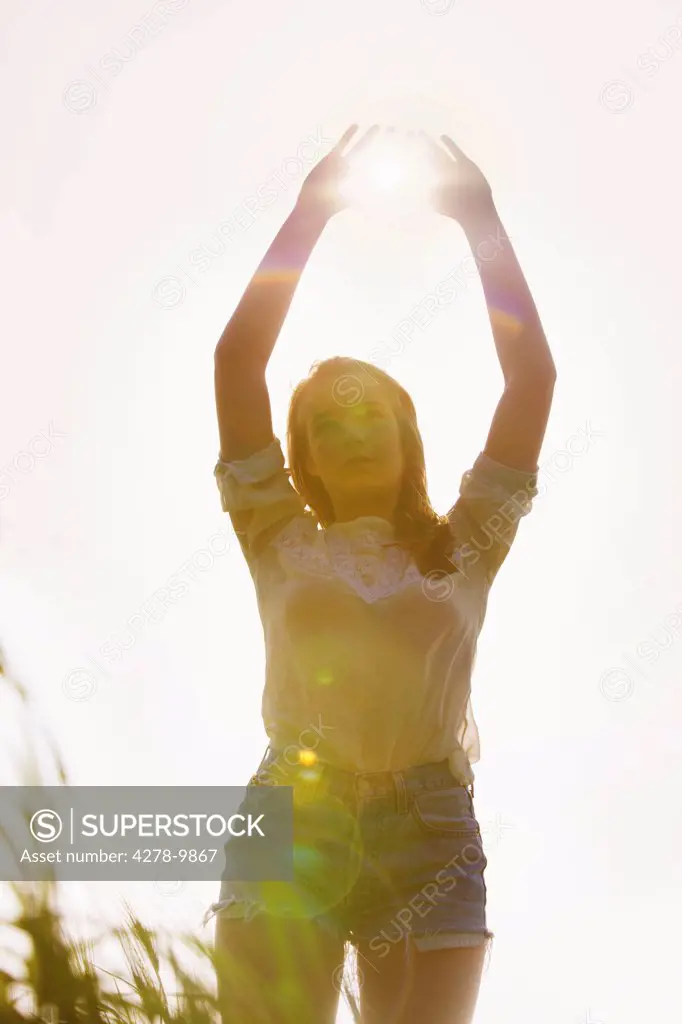 Young Woman Standing in a Field with Sun Shining through her Hands