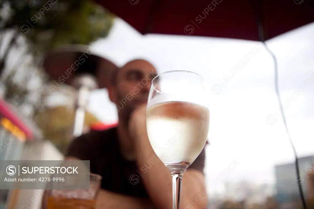 Man Sitting at Outdoor Bar with Glass of White Wine in Foreground