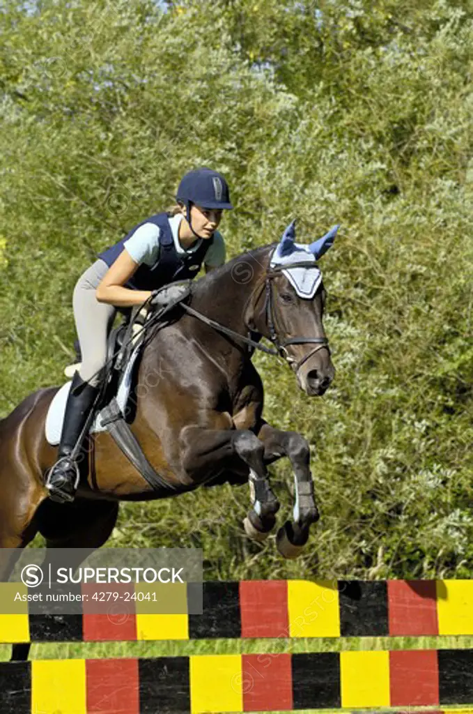 Young lady wearing a body protector and a riding hat while jumping