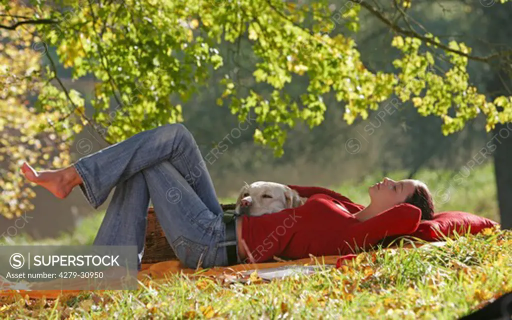 young woman with Labrador Retriever dog - lying under tree