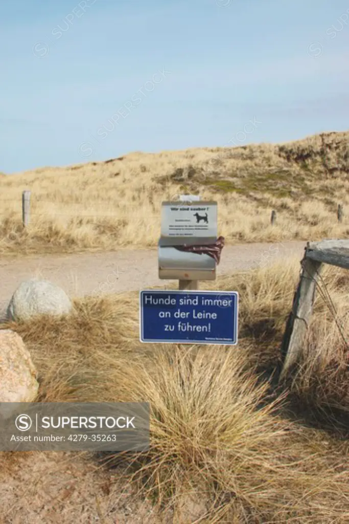 beach: dog waste bag dispenser and sign 'leash dogs'