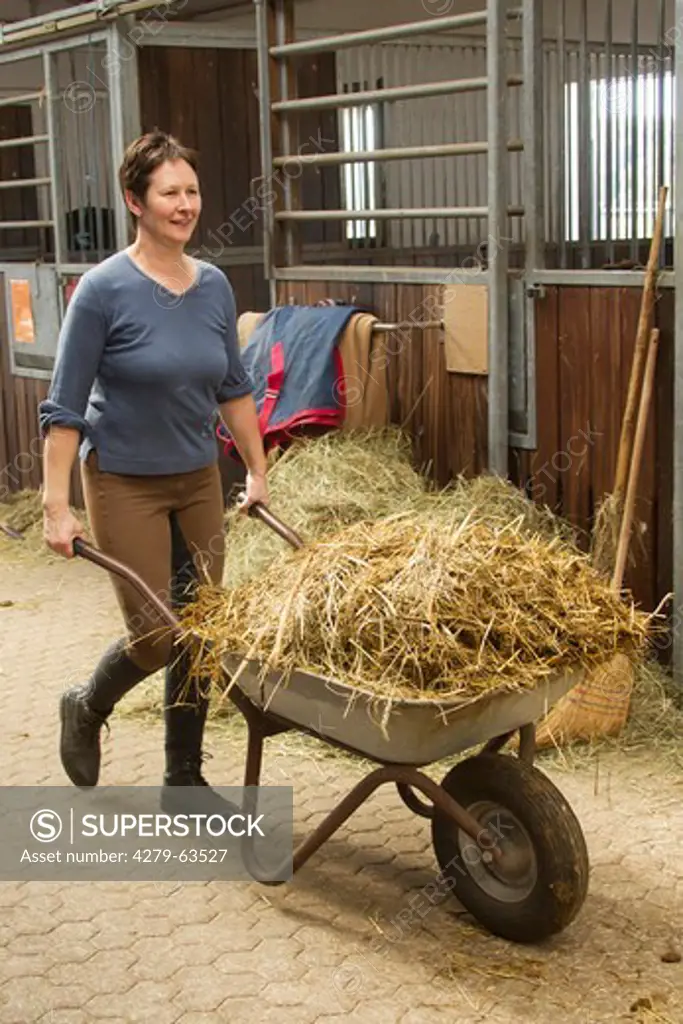 Woman pushing a cart with fresh straw in a stable