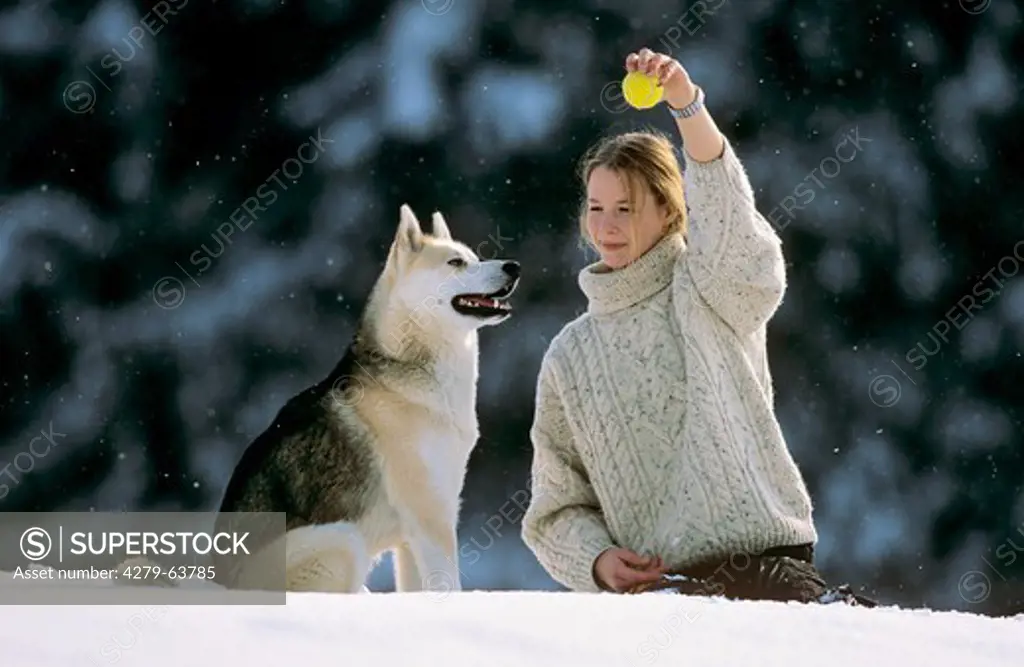 Girl playing with her Siberian Husky with a ball in snow