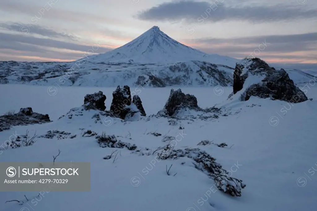 Lava outcrops on the shore of Kronotskoye Lake with Kronotsky Volcano in background. Kamchatka, Russia