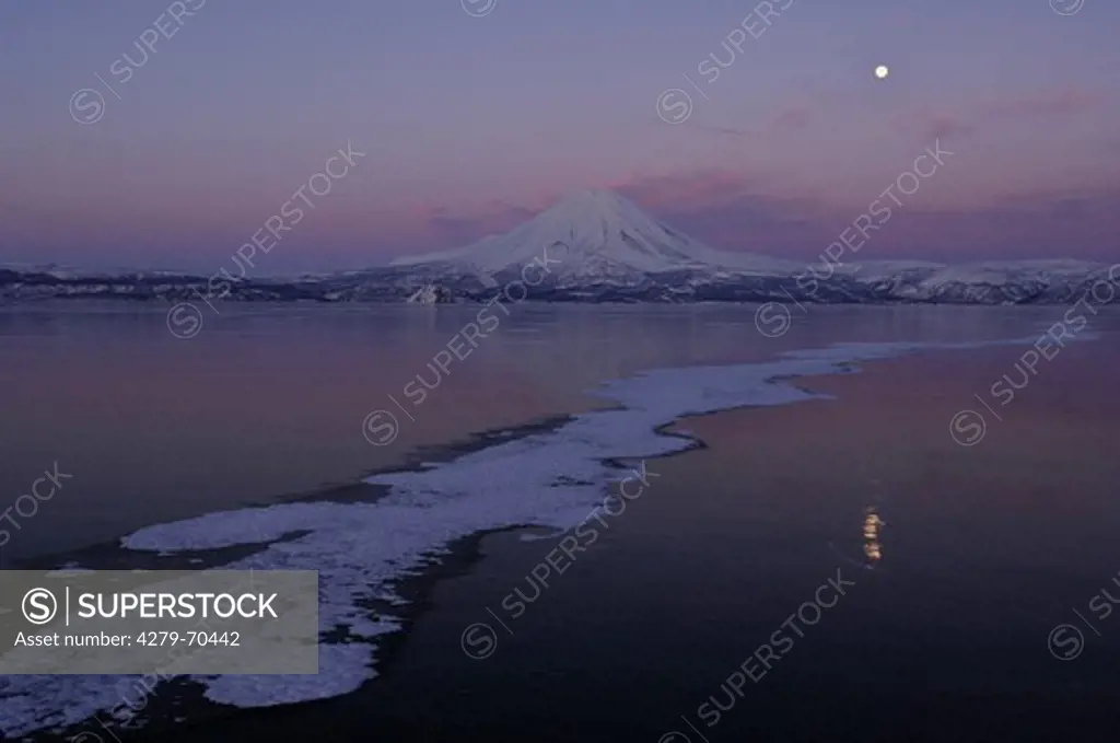 Frozen Kuril Lake with Ilinsky Volcano rising in the backdrop at dusk. Southern Kamchatka Wildlife Refuge, Kamchatka, Russia