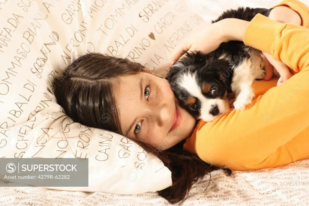 girl with Cavalier King Charles Spaniel puppy - smooching in bed