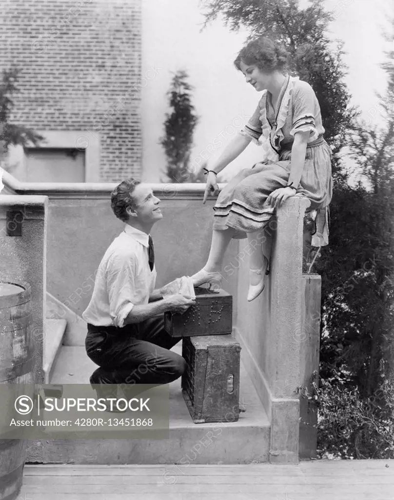 Woman sitting on a ledge having her shoes cleaned by a man All persons depicted are not longer living and no estate exists Supplier warranties that th...