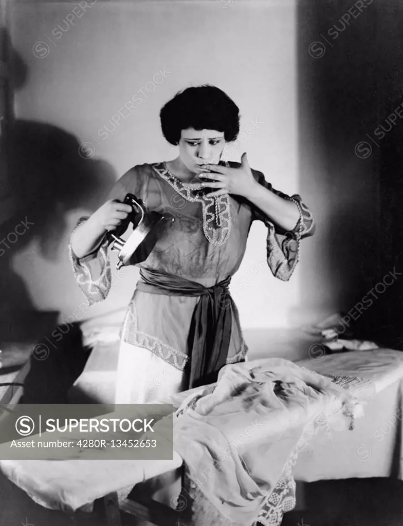 Woman with a finger in her mouth after she burned herself with an iron All persons depicted are not longer living and no estate exists Supplier warran...