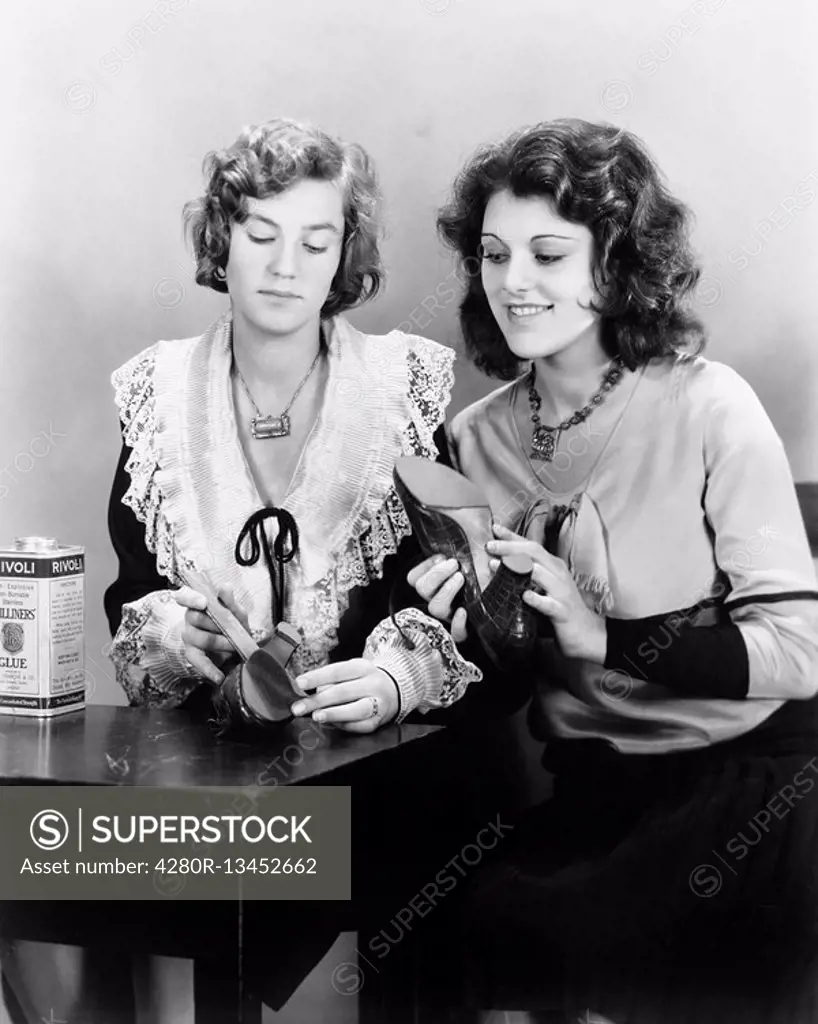 Two woman sitting together at a table repairing their shoes All persons depicted are not longer living and no estate exists Supplier warranties that t...