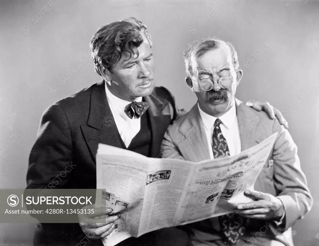 Two mature men reading a newspaper together All persons depicted are not longer living and no estate exists Supplier warranties that there will be no ...