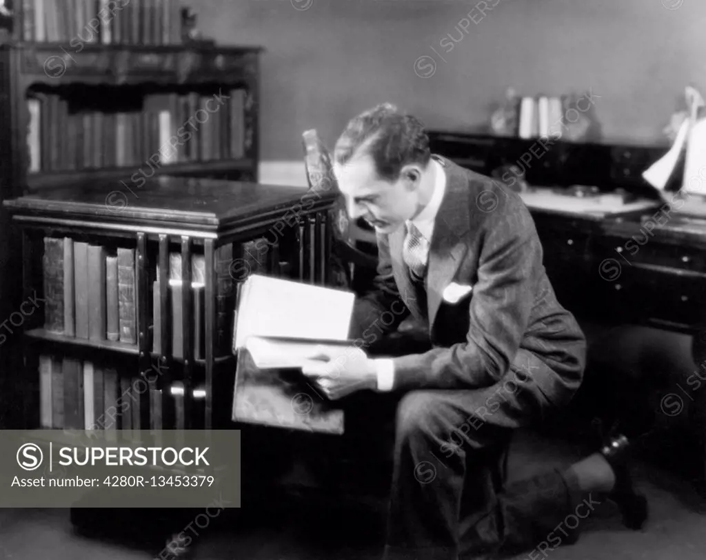 Man kneeling in his home library browsing a book All persons depicted are not longer living and no estate exists Supplier warranties that there will b...