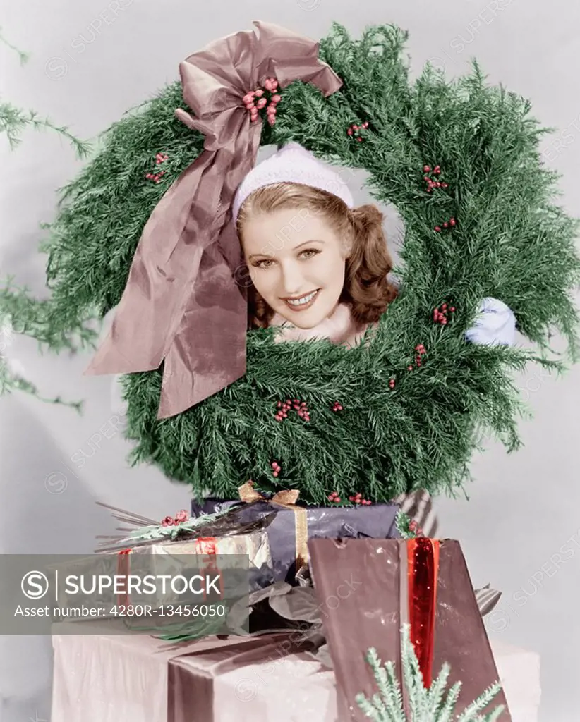 Young woman looking through a wreath with presents in front of her Old Visuals