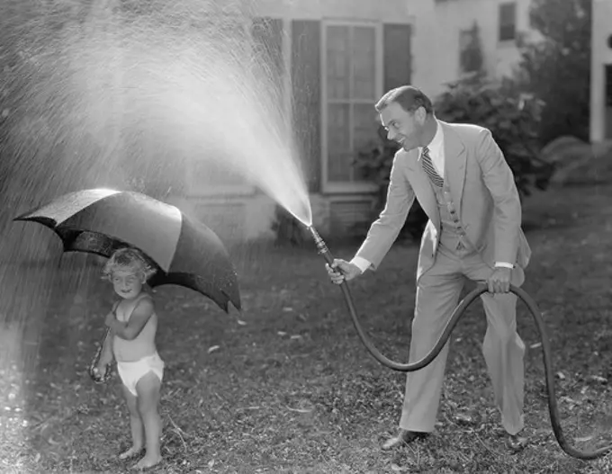 Toddler and dad playing with hose in yard