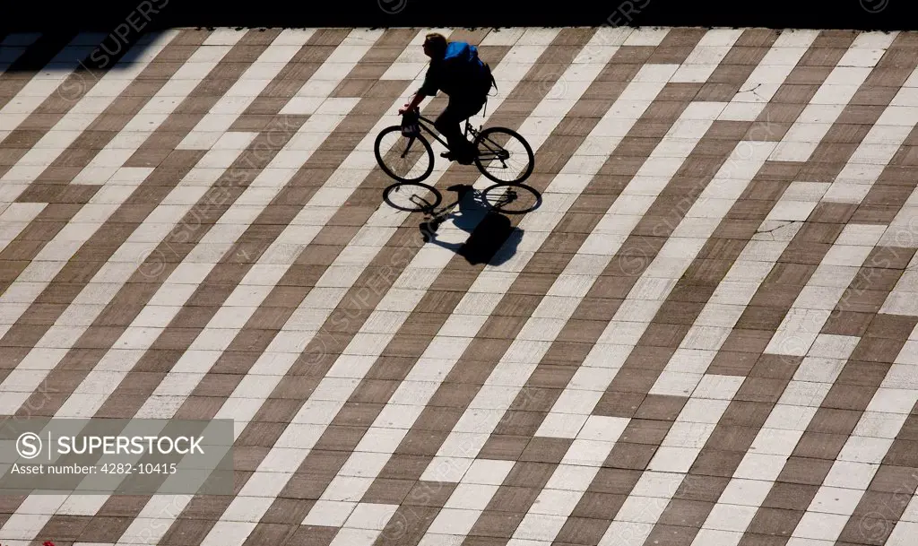 England, West Midlands, Birmingham. A man cycling across the footpath from Paradise Circus to Centenary Square.