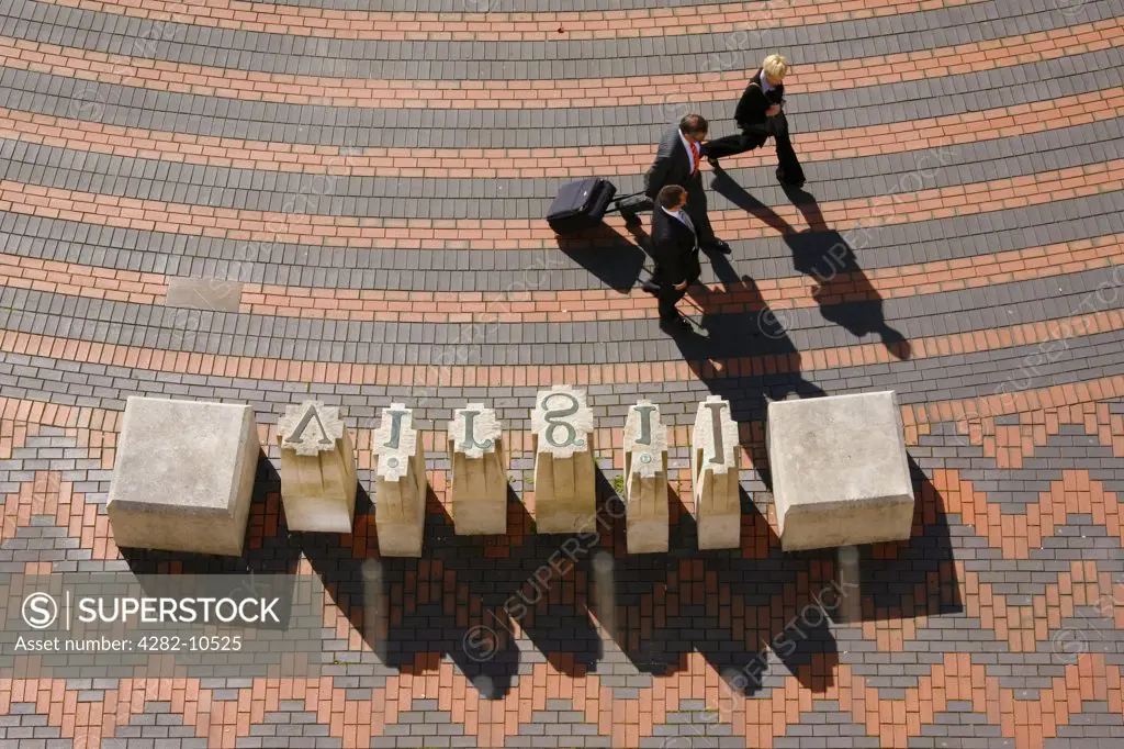 England, West Midlands, Birmingham. Business people walking past the Portland stone sculpture, Industry and Genius, by David Patten, that stands in Centenary Square.