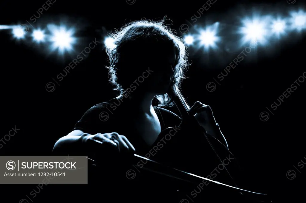 England, West Midlands, Birmingham. A cellist performing on stage, backlit by theatre lights.