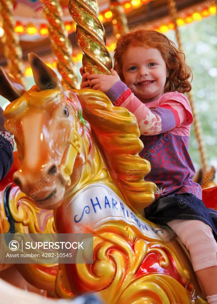 England, West Midlands, Birmingham. A young girl enjoying a ride on a fairground carousel horse.