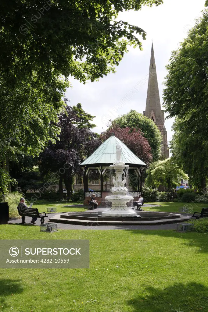 England, Worcestershire, Redditch. People relaxing in Church Green in the centre of Redditch by a fountain, bandstand and St. Stephen's Church.