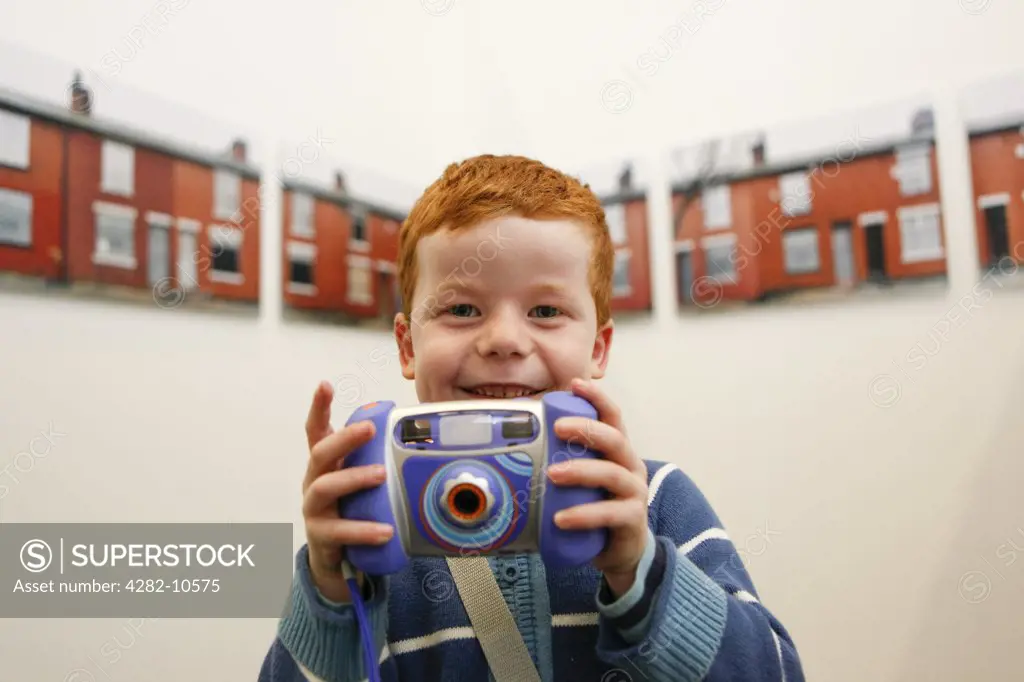 England, West Midlands, Walsall. A happy young red haired boy holding a childrens camera in The New Art Gallery Walsall.