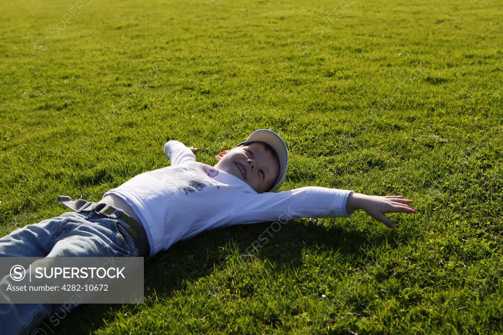England, West Midlands, Birmingham. A young boy lying on grass in the sunshine.