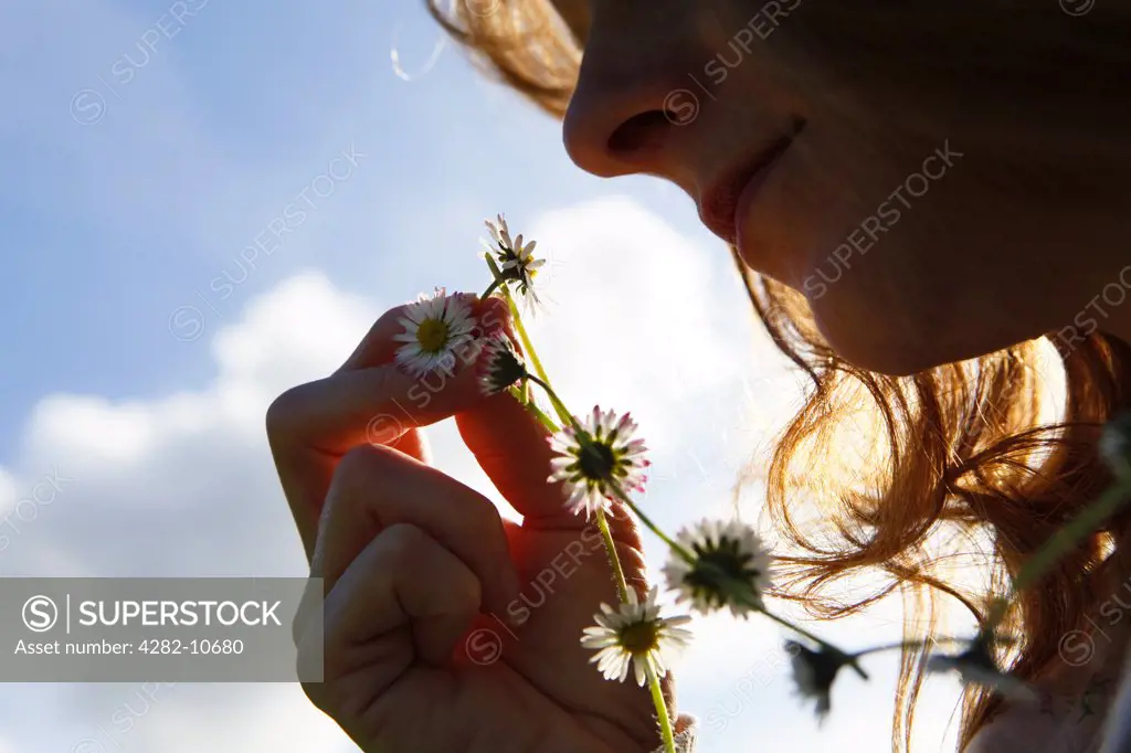 England, West Midlands, Birmingham. A woman holding up a daisy from the daisy chain she is wearing around her neck.