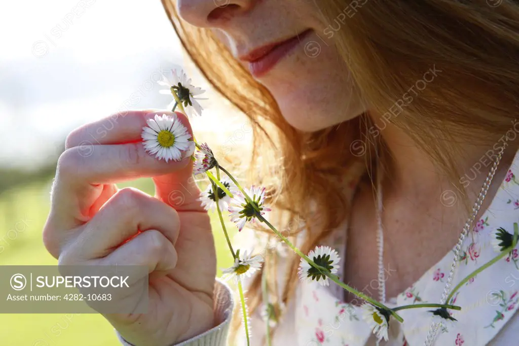 England, West Midlands, Birmingham. A woman holding up a daisy from the daisy chain she is wearing around her neck.