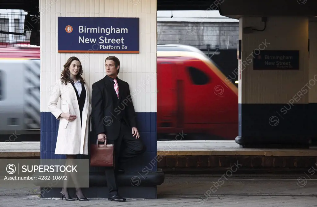 England, West Midlands, Birmingham. A business man and woman standing on a platform at Birmingham New Street station waiting for a train.