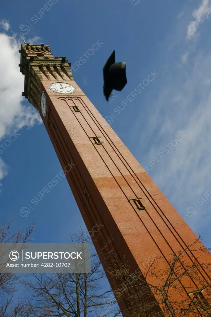 England, West Midlands, Birmingham. A mortarboard thrown high into the air in front of the Joseph Chamberlain Memorial Clock Tower, known as 'Old Joe', in the centre of the University of Birmingham campus.