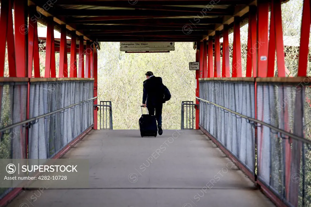 England, Shropshire, Telford. A businessman with luggage crossing the footbridge at Telford Central railway station.