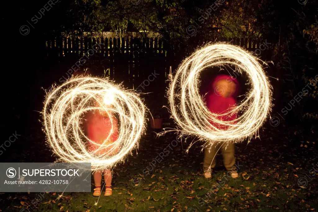 England. Children creating circles of light with sparklers in a garden.