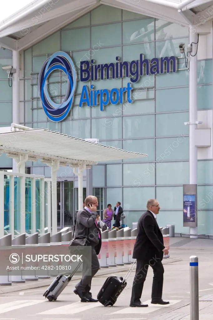 England, West Midlands, Birmingham. Businessmen crossing a zebra crossing with their baggage outside Birmingham Airport.