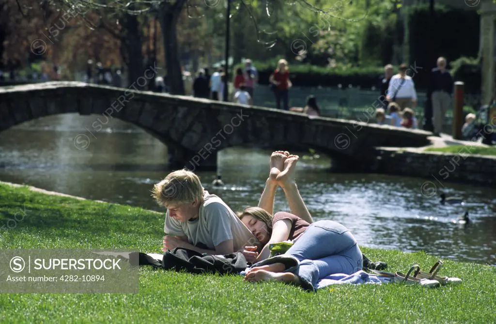 England, Gloucestershire, Bourton-on-the-Water. Lazy days on the riverbank at Bourton-on-the-Water.