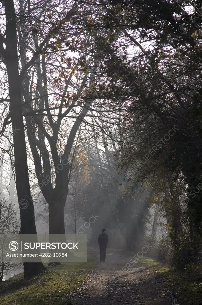 England, Oxfordshire, Oxford. Man walking by the banks of the River Cherwell.