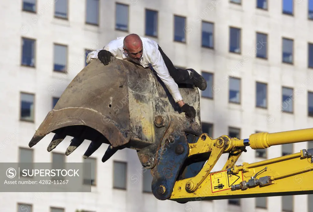 England, London, South Bank. A man clings to a mechanical digger as part of Transports Exceptionnels performance art.