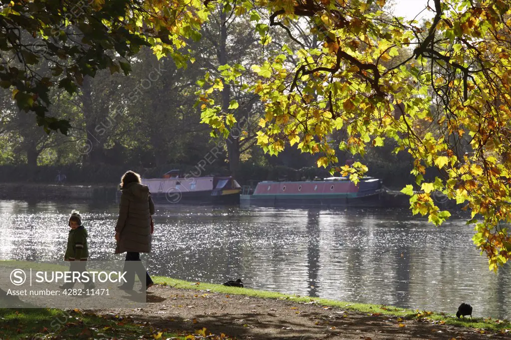 England, Oxfordshire, Oxford. Mother and child walking along a path by the River Thames at Oxford, in Autumn.